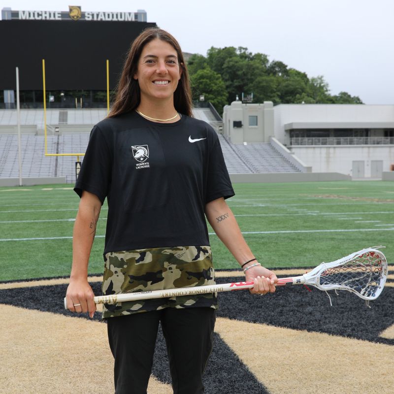 Professional Lacrosse player Michele Tumolo holding a lacrosse stick while posing at a stadium