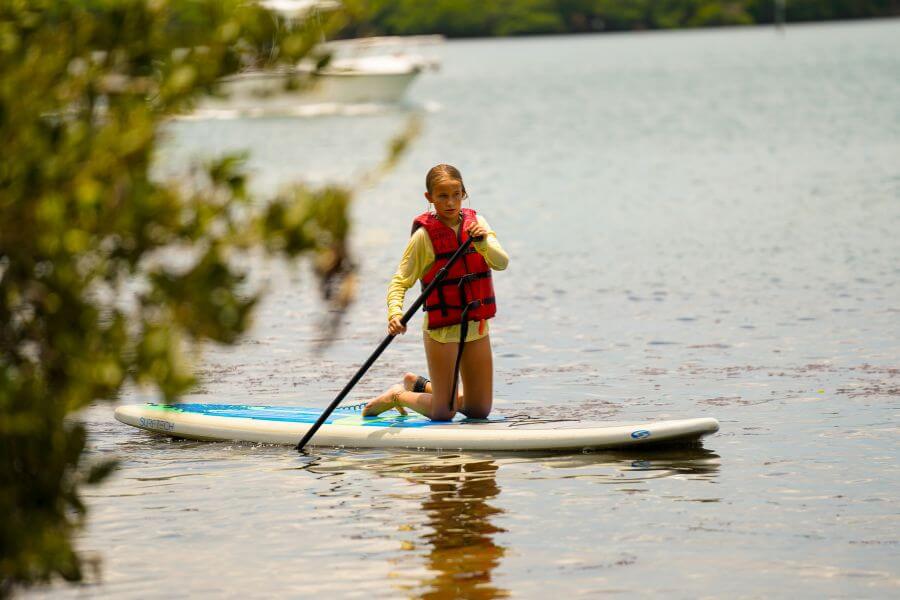 Young girl kneeling on a stand up paddleboard while rowing on the water