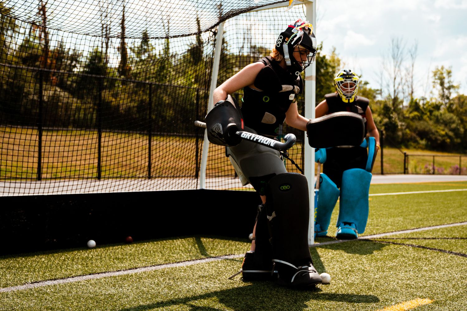 Two field hockey goalies standing in front of the goal box