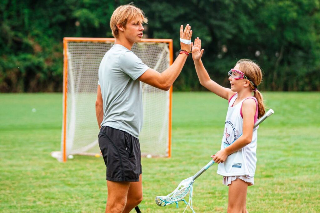 a young lacrosse player high fives her coach after a great practice at lacrosse camp