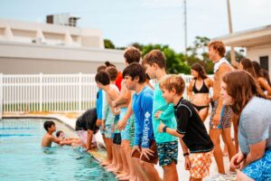 A group of boys excitedly stand at the edge of a swimming pool while at sports camp