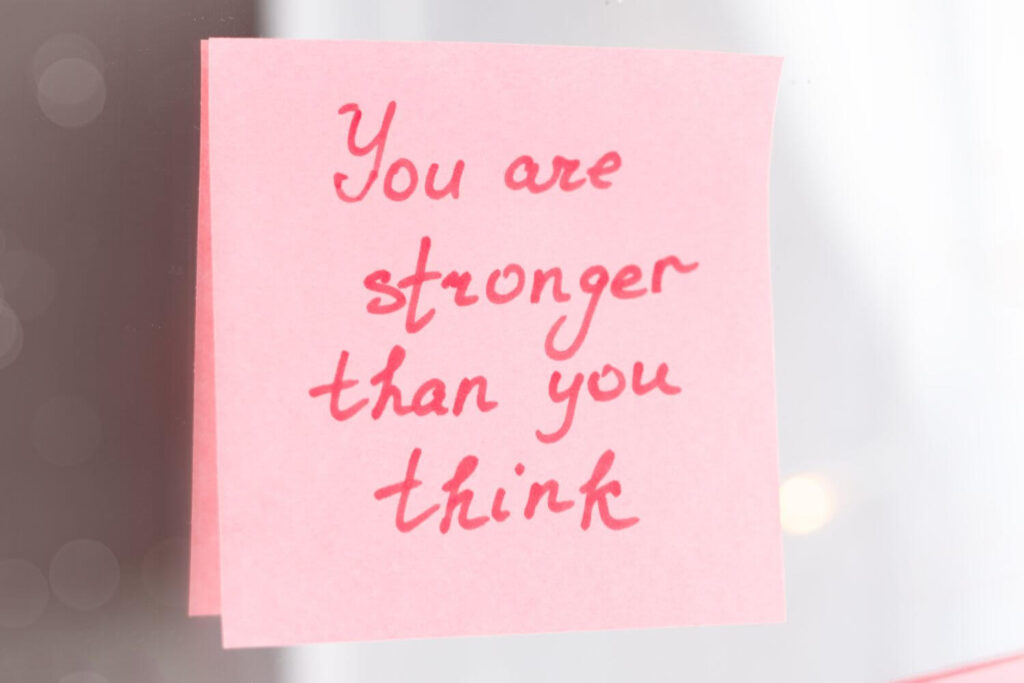 A pink post-it note with red text "You are stronger than you think" written is placed on a  mirror