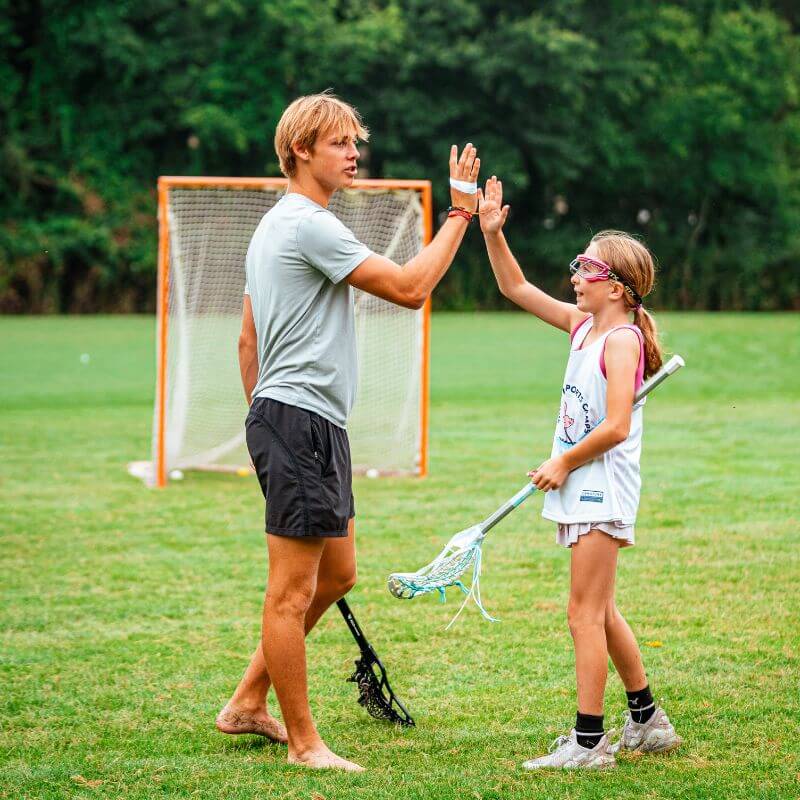 A lacrosse coach high fives a lacrosse player on the field