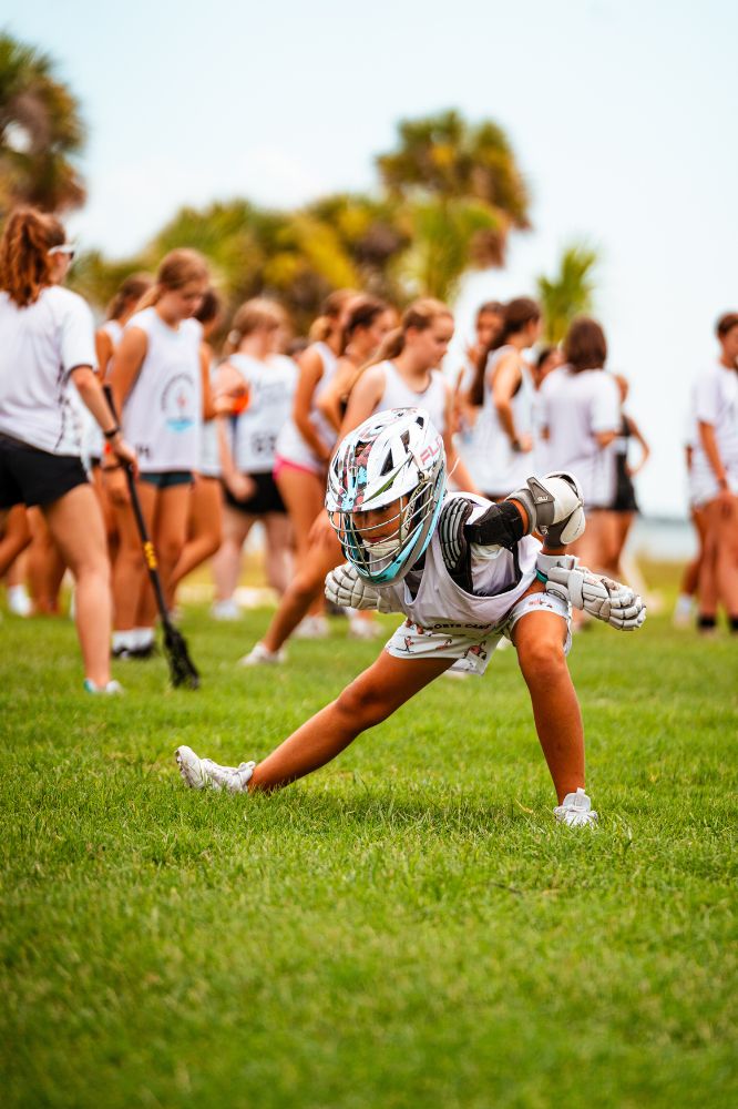 Young lacrosse player wearing pads and helmet stretching before a scrimmage at sports camp