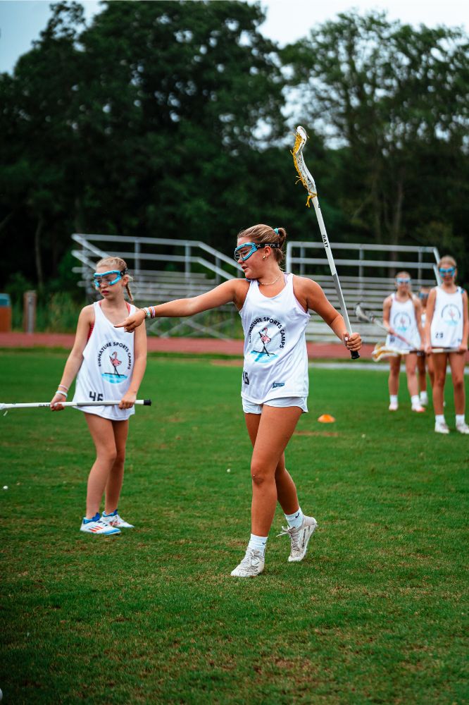 Lacrosse camper assisting another athlete during practice at overnight sports camp