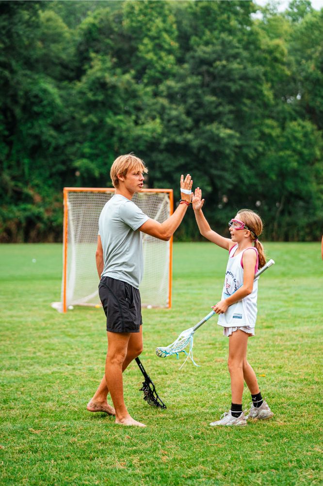 Lacrosse coach high fiving a young lacrosse player during practice