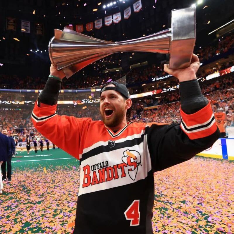 Buffalo Bandits professional lacrosse player Ian MacKay holding a trophy above his head in celebration of winning lacrosse championship