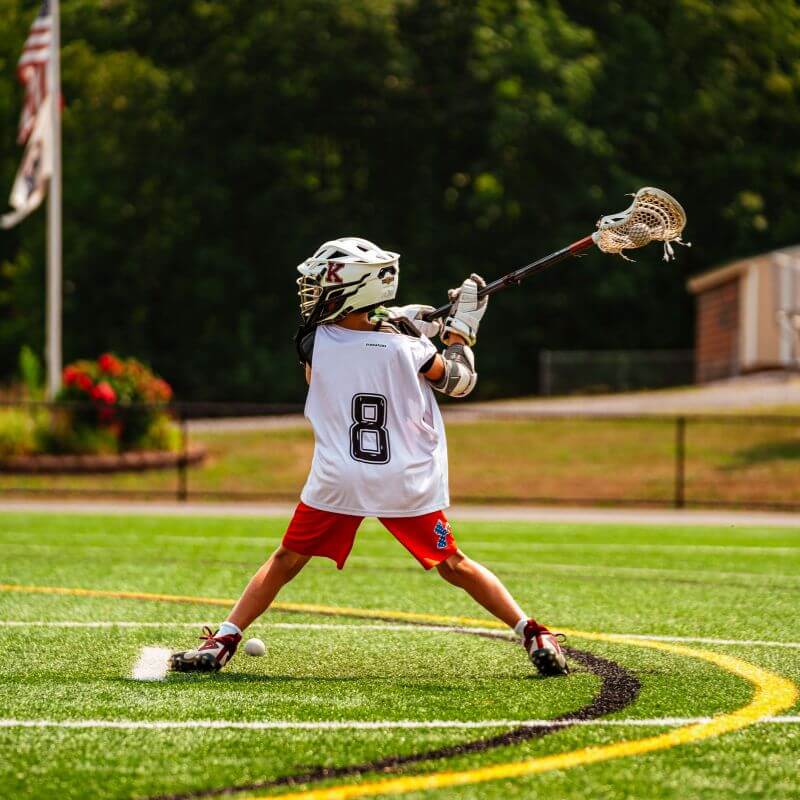 Boy wearing number 8 jersey shooting during lacrosse practice at summer camp