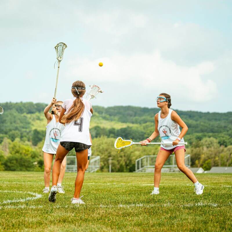 Three girls in action during a lacrosse scrimmage at overnight sports camp