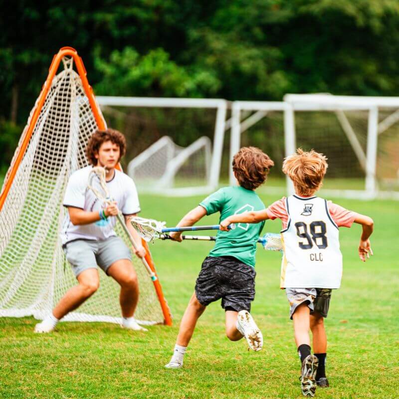 young lacrosse players running towards goalie during lacrosse 3v3 tournament at sports camp