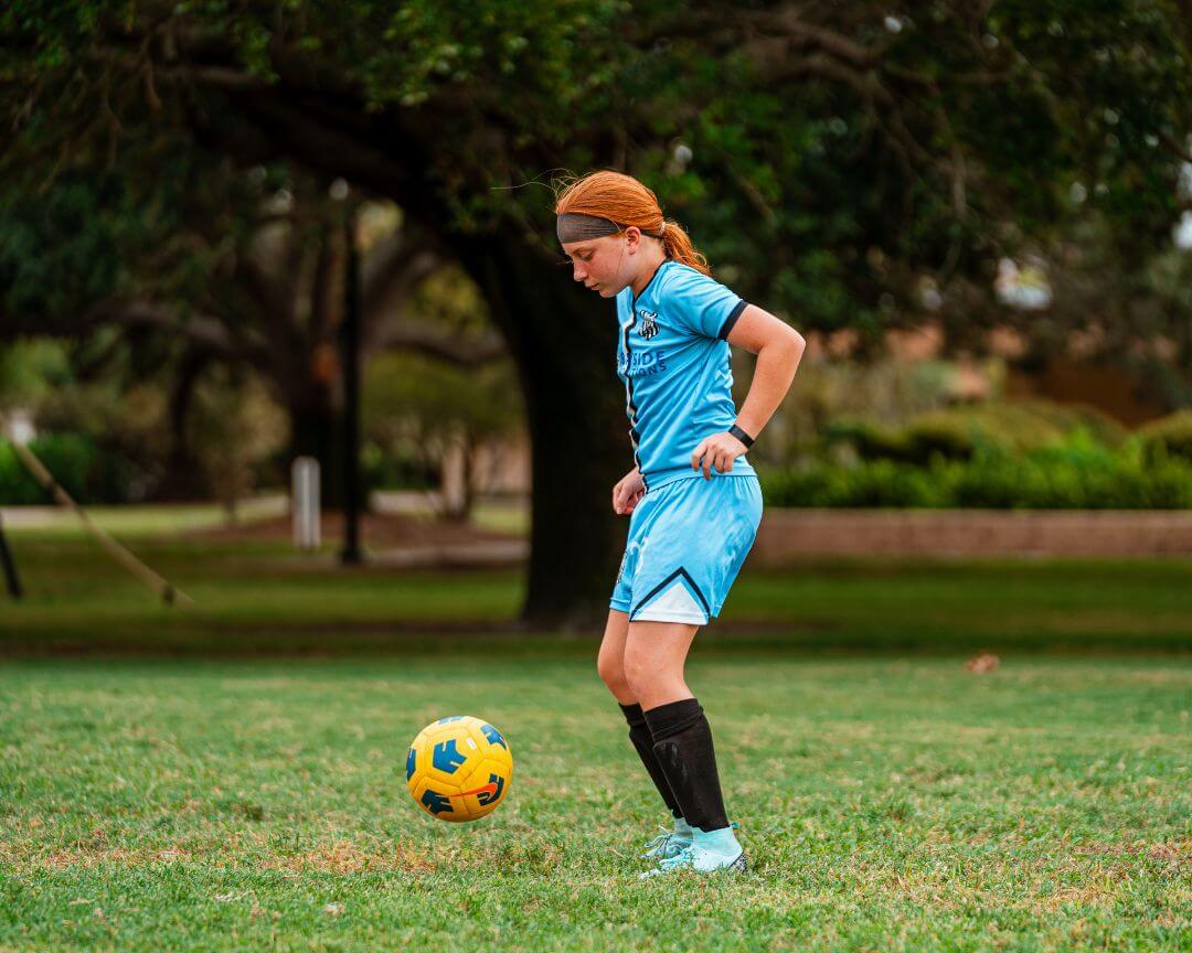 Girl in blue soccer uniform dribbling a yellow soccer ball at signature sports camps