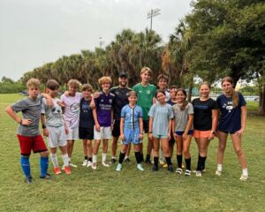Group of youth athletes at soccer camp pose for a photo with pro soccer player Nicky Law after practice