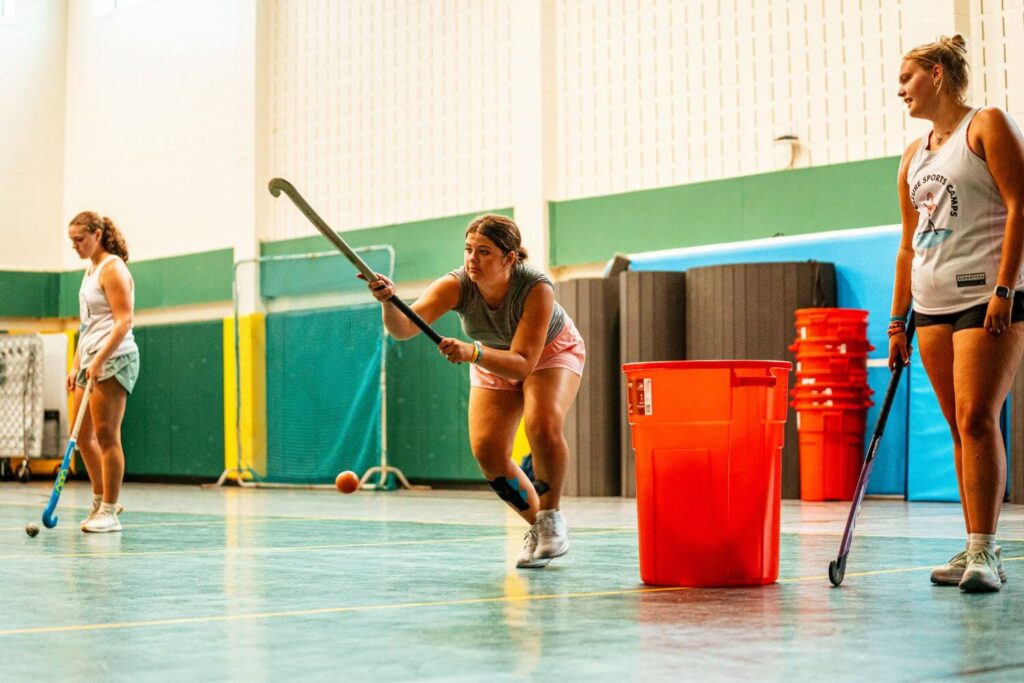 Girls at signature sports camp look on as a coach demonstrates field hockey drills at practice