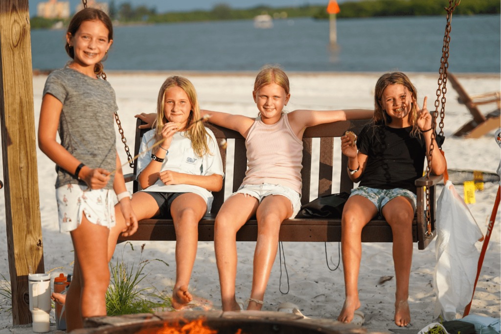 Four girls at overnight sports camp surrounding a bonfire on the beach as they roast marshmallows