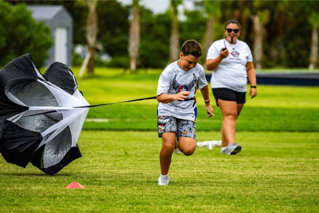 Boy at overnight sports camp doing speed parachute drills as a coach watches him