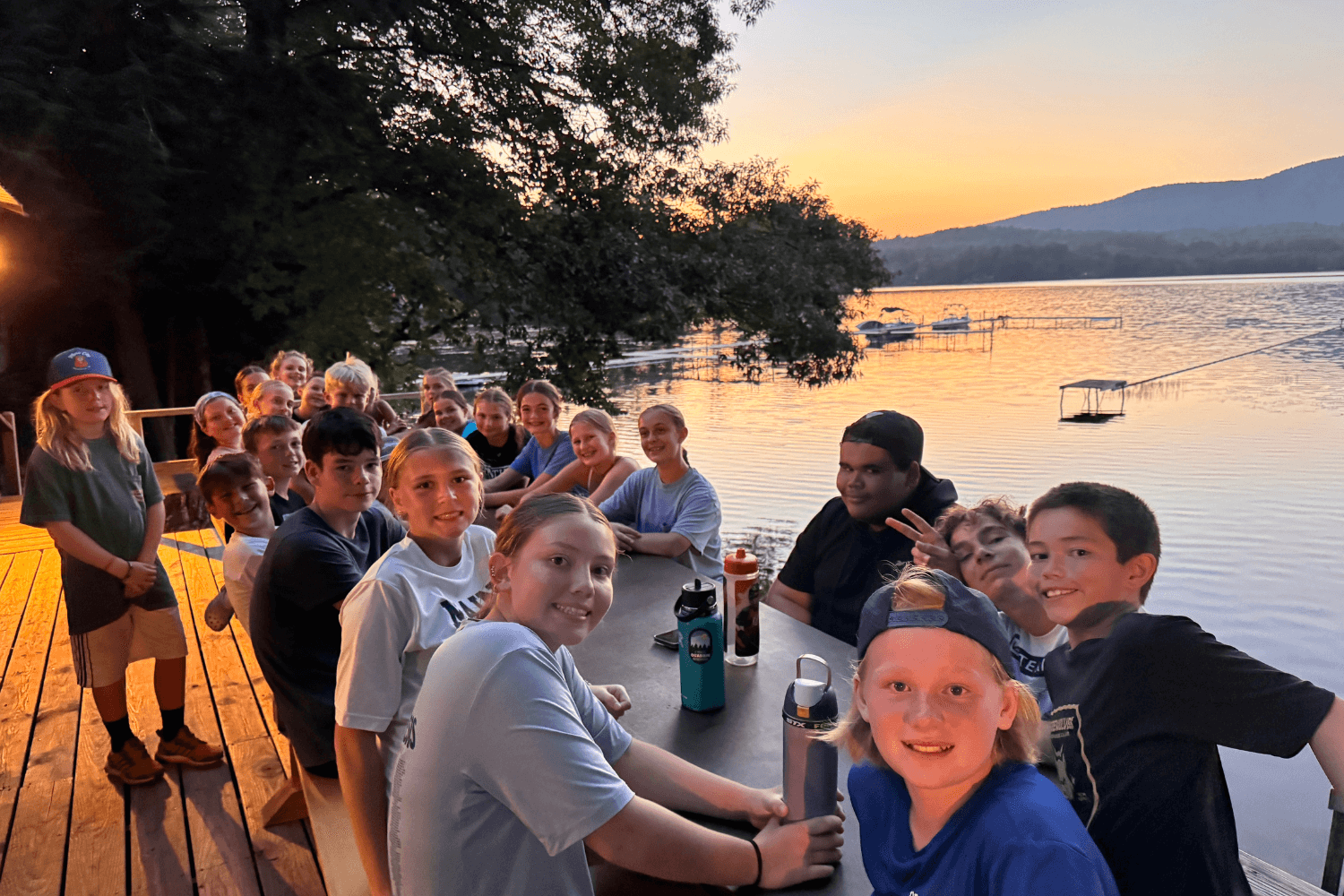 Kids at sports camp gathered around a waterfront table during a sunset