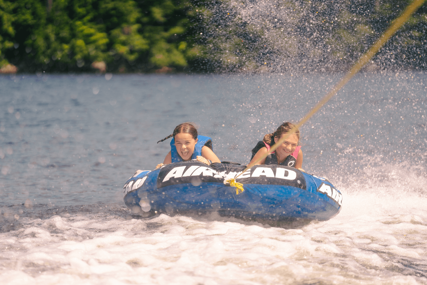 Two girls smiling while tubing on the lake at overnight sports camp