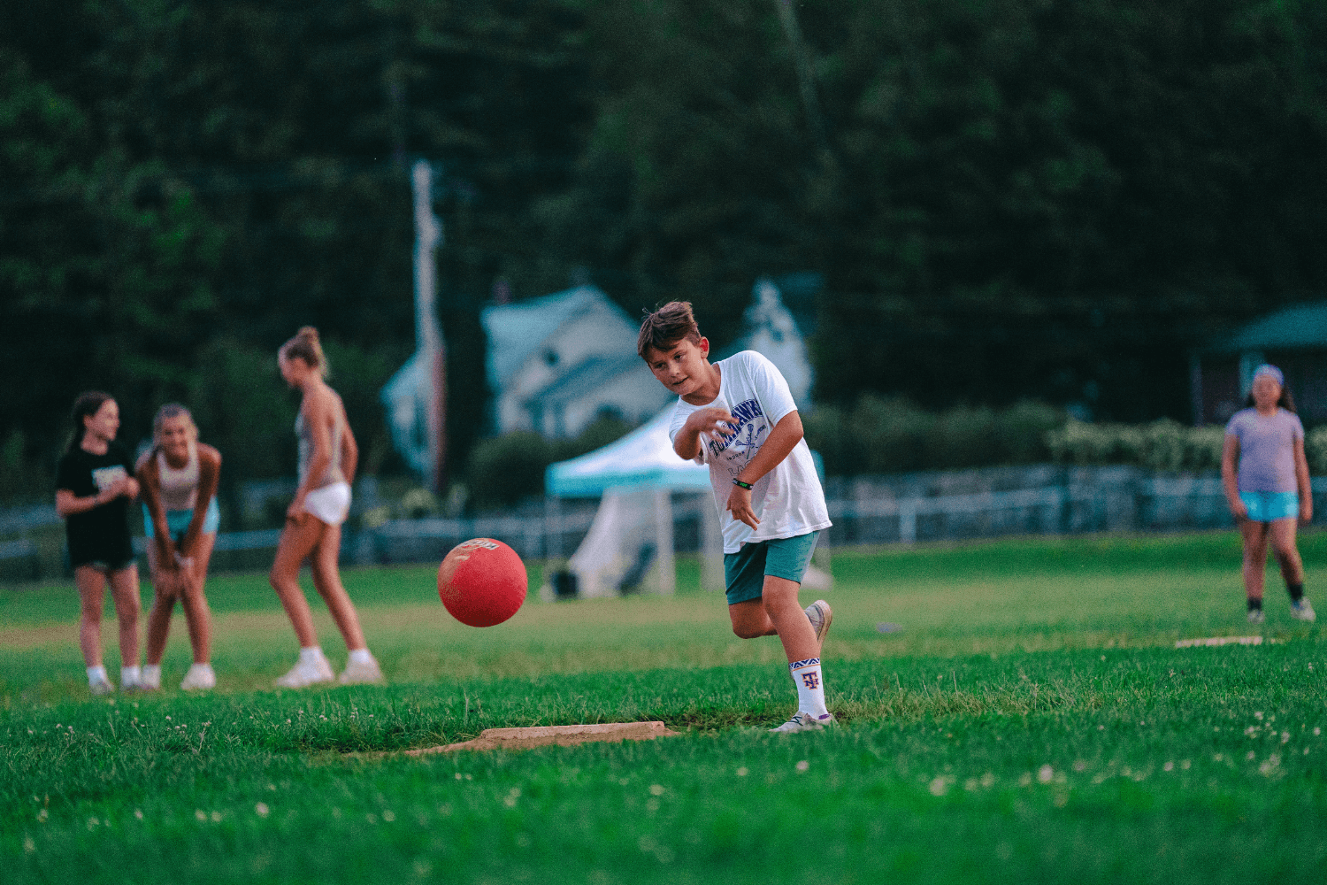 Boy pitching a kickball during a co-ed game at camp