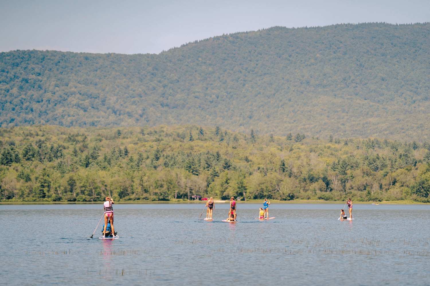 Distant view of girls stand up paddleboarding on the lake at camp