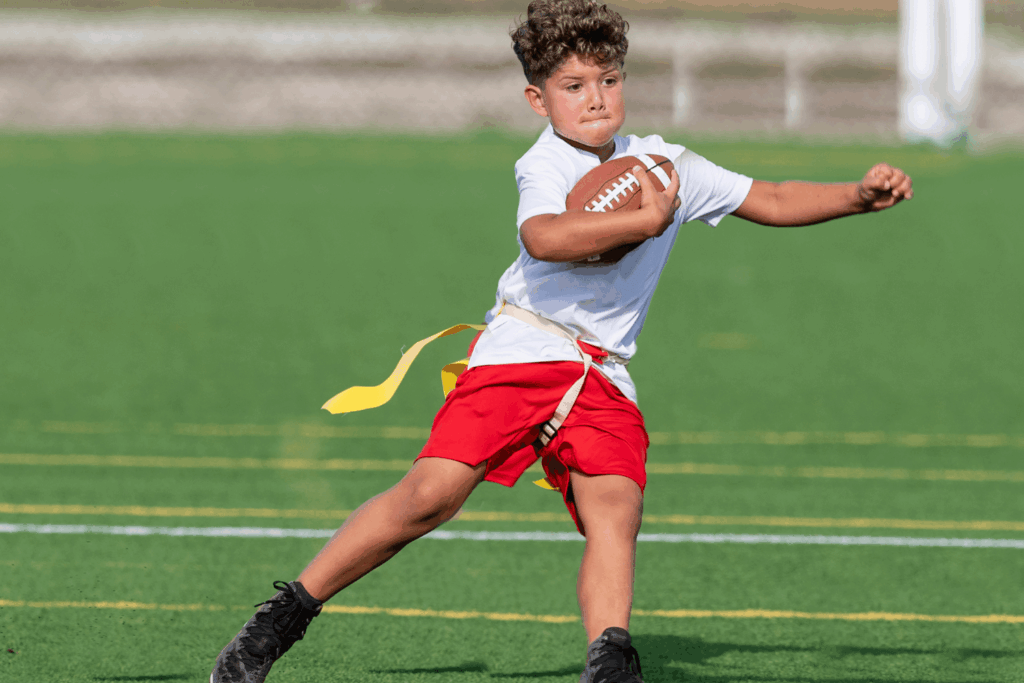 Boy in red shorts and white shirt with yellow football flag holding a football