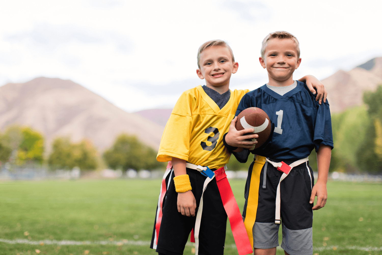 Two boys smiling holding a football after a flag football game