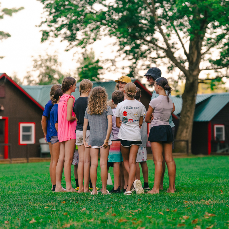 Kids huddled in a circle speaking with a coach during sports camp