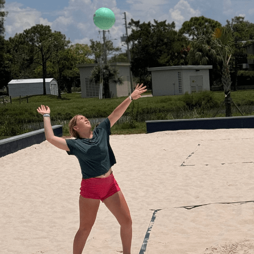 Girl serving volleyball during a game of beach volleyball