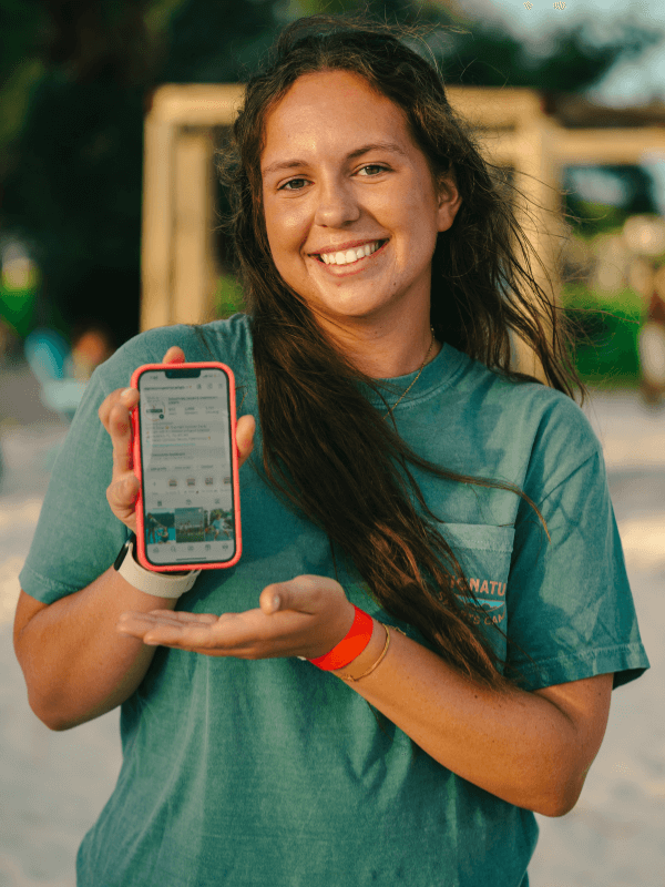 Signature Sports Camps Counselor in Training smiling for the camera while holding a cell phone showing Signature's Instagram account