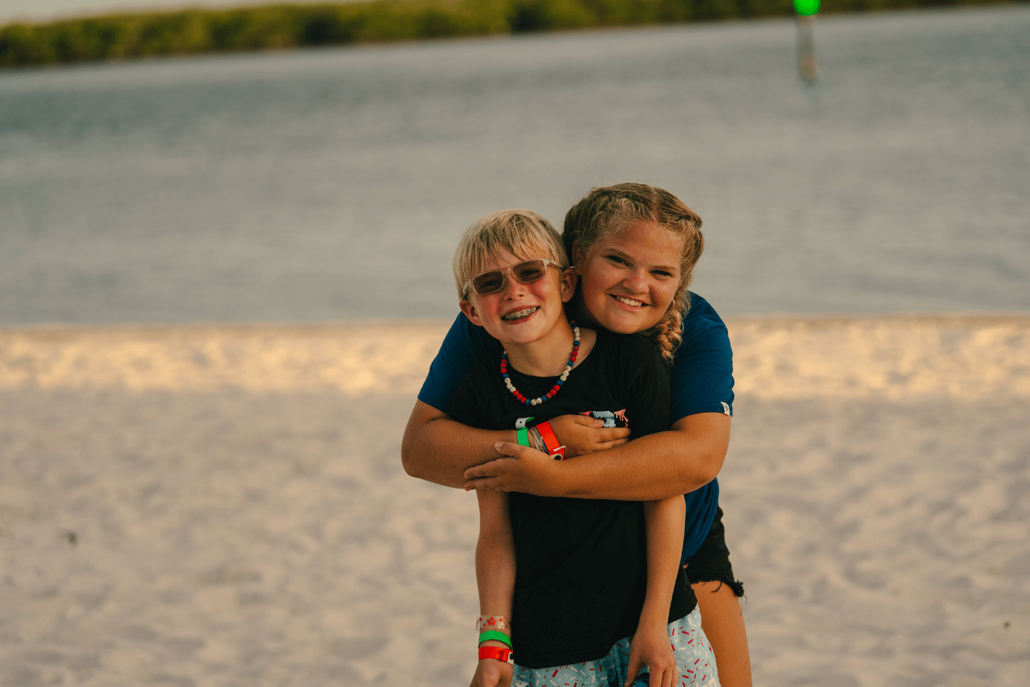 A girl is wrapping her arms around a boy as they smile for a photo on the beach at Signature Sports Camps in Florida