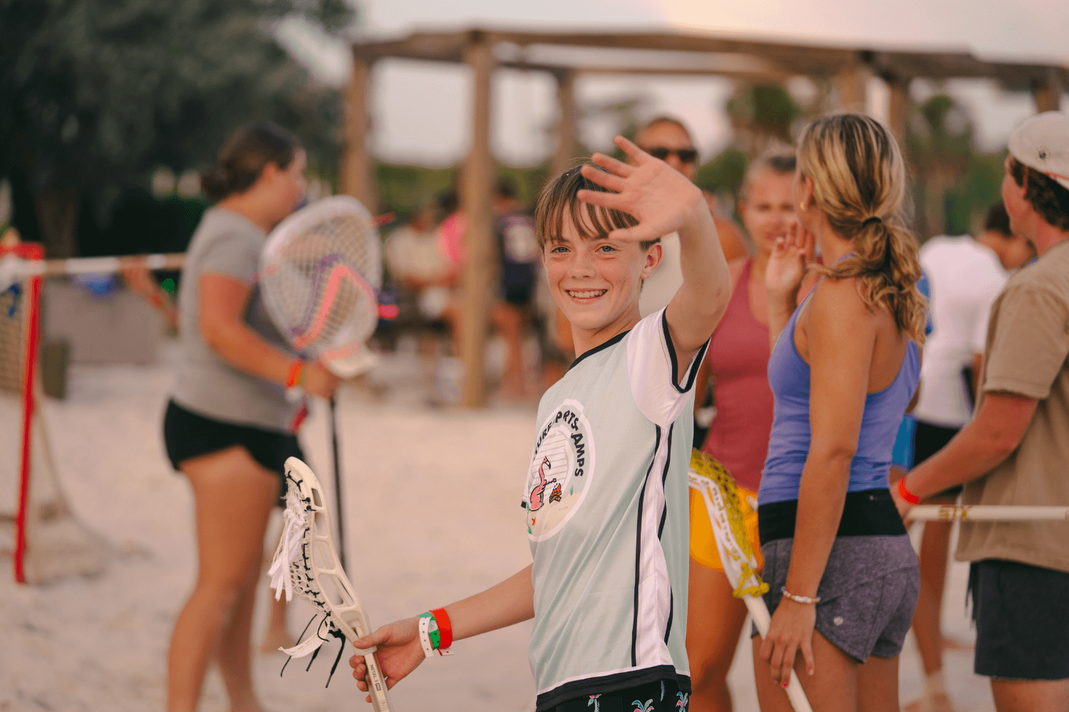 Boy on the beach at summer sports camp waves and smiles for a photo
