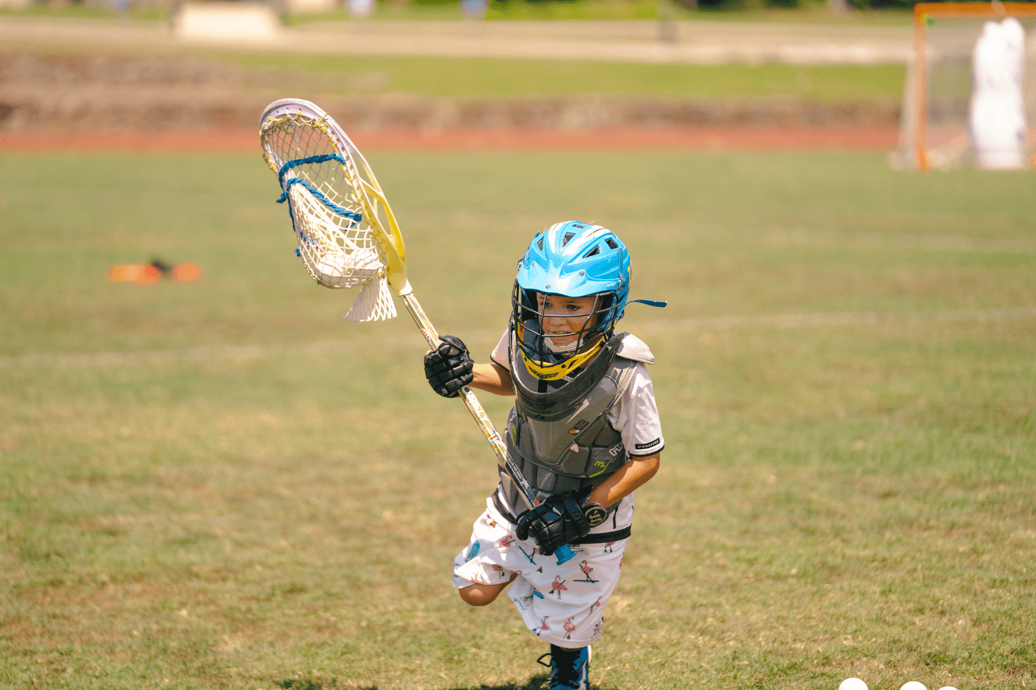Boy running with lacrosse stick while in full pads during summer sports camp