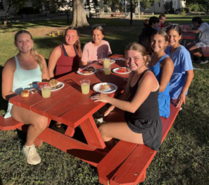 Group of young female athletes sitting together at a picnic table enjoying healthy, energizing snacks. Reflecting the nutrition reset tips for staying fueled and balanced over the holiday break.