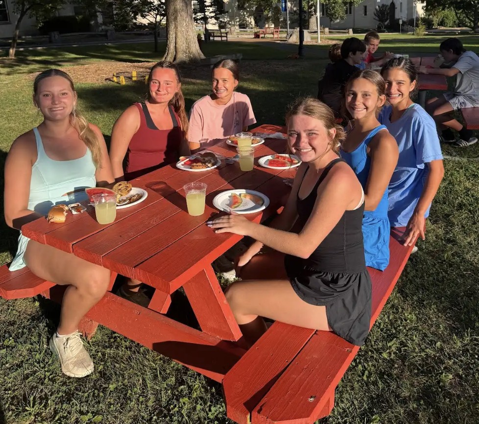 Group of young female athletes sitting together at a picnic table enjoying healthy, energizing snacks. Reflecting the nutrition reset tips for staying fueled and balanced over the holiday break.