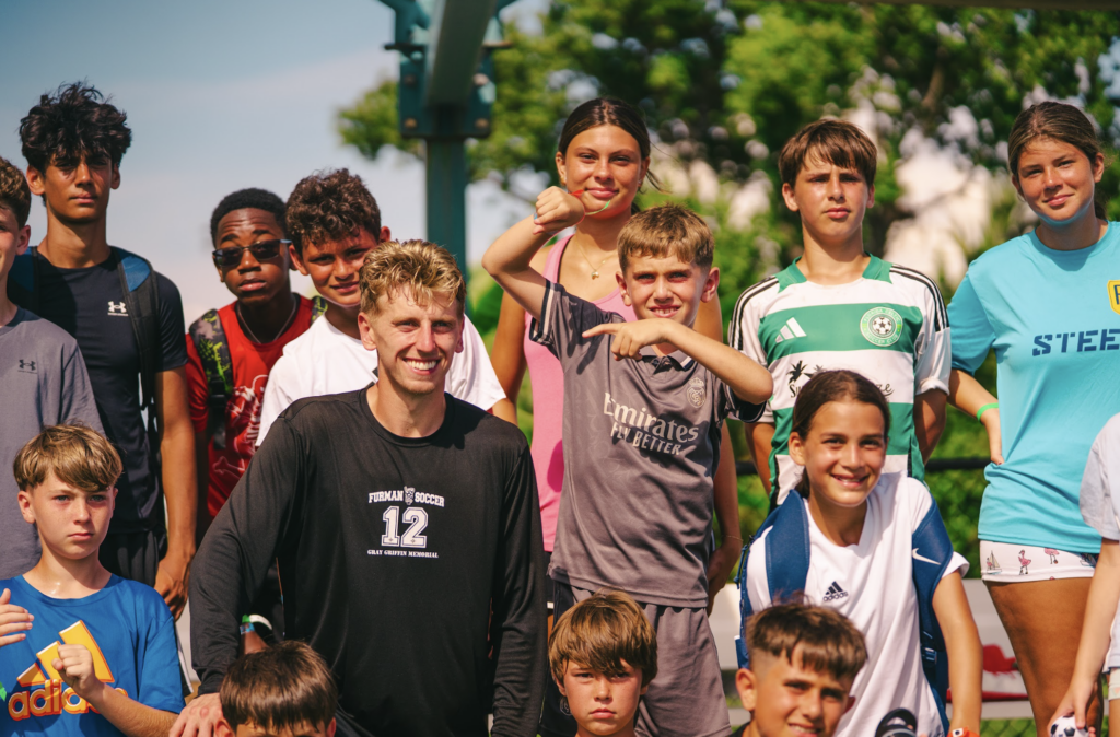 Kids at signature sports camps stand next to a professional soccer player who came to coach them.
